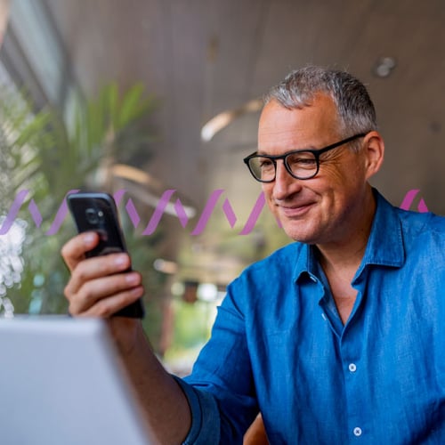 Future of Networks Blog (Spain) Thumbnail Photo of a smiling, casually dressed man reading something on his cellphone. In the background, a series of small purple wave forms run across the frame, representing communications.